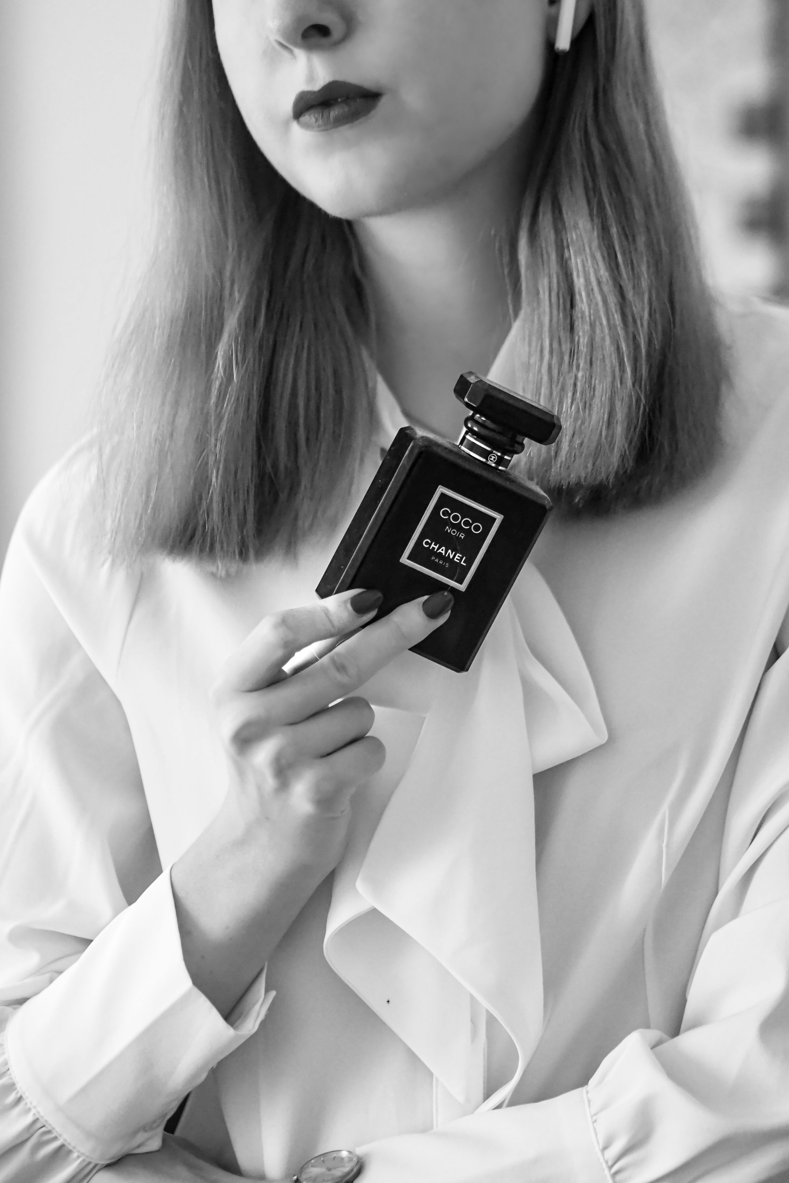 Foto em preto e branco de uma mulher estilosa segurando um frasco de perfume Chanel.
