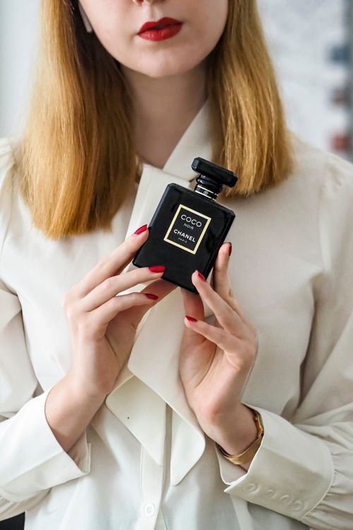 Free Stylish woman in white blouse holding luxury perfume indoors. Stock Photo