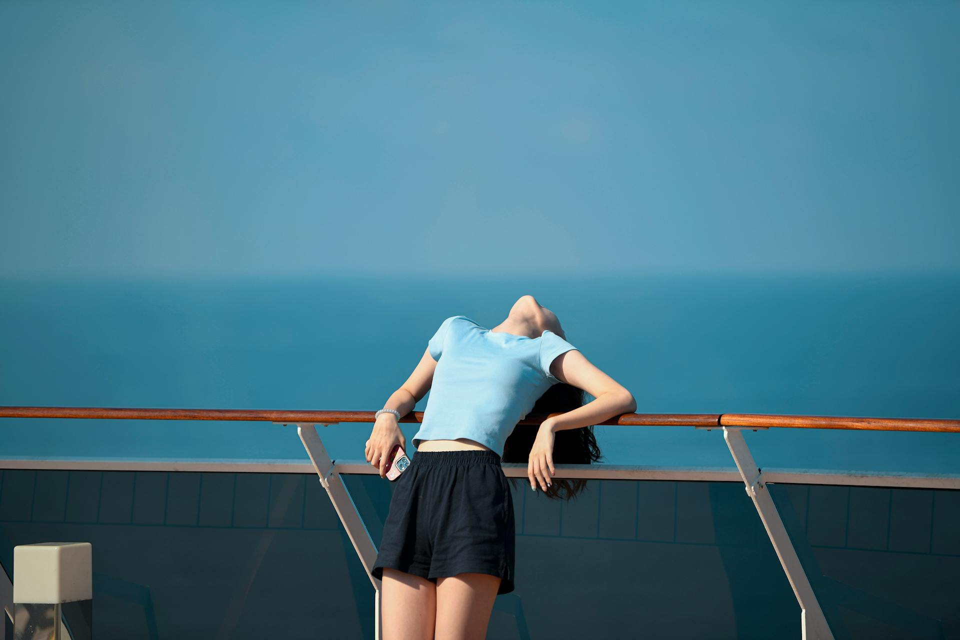 Woman enjoying the sea breeze on a cruise ship deck with clear blue sky.