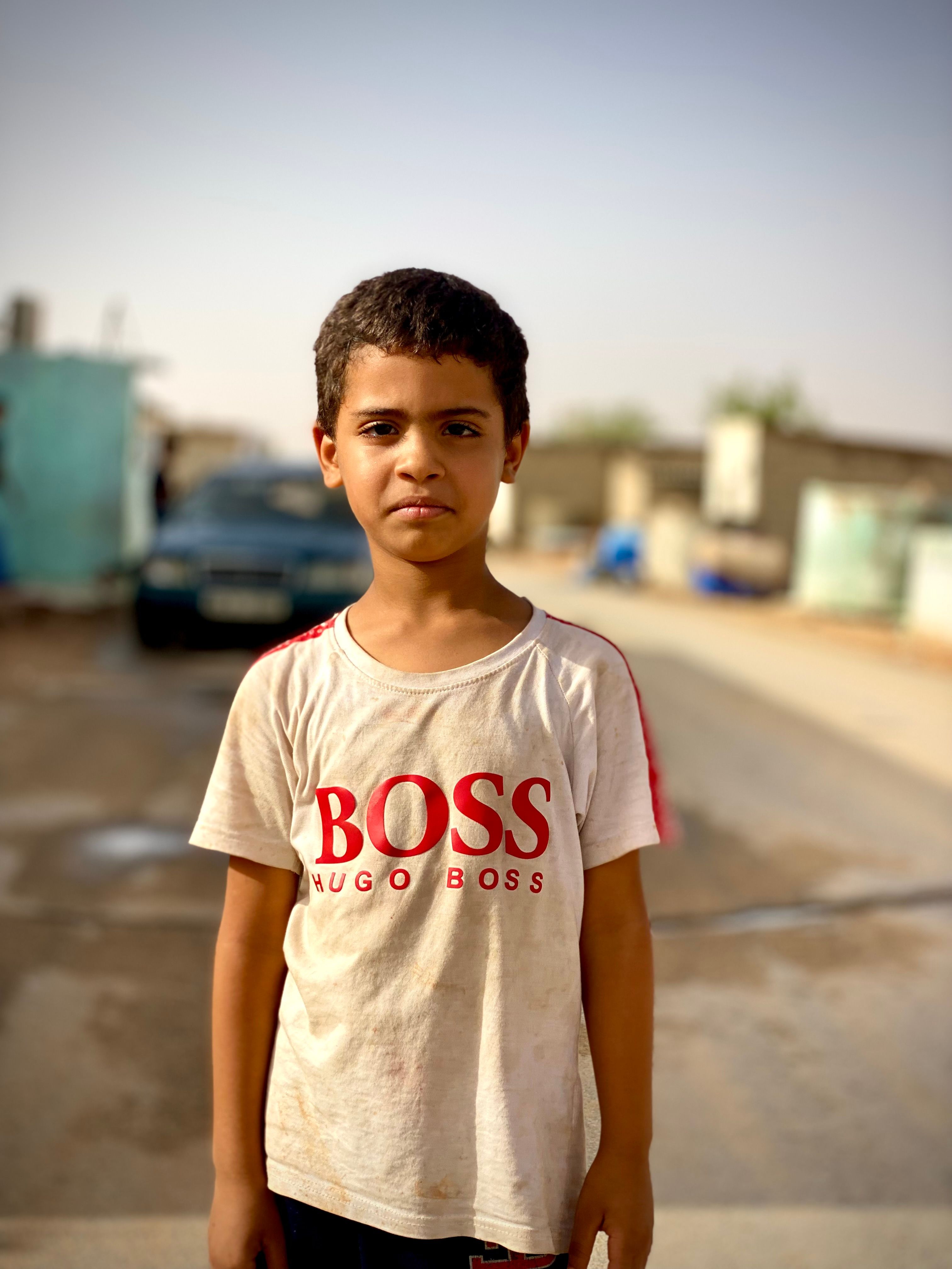 A young boy stands in a sunlit street in Tindouf, Algeria, exuding strength and resilience.