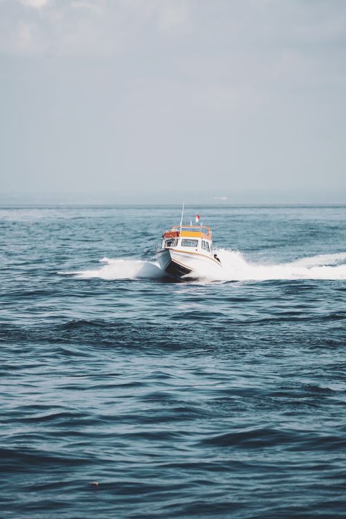 Free A speedboat cutting through the ocean near Bali, Indonesia, creating waves under a clear sky. Stock Photo