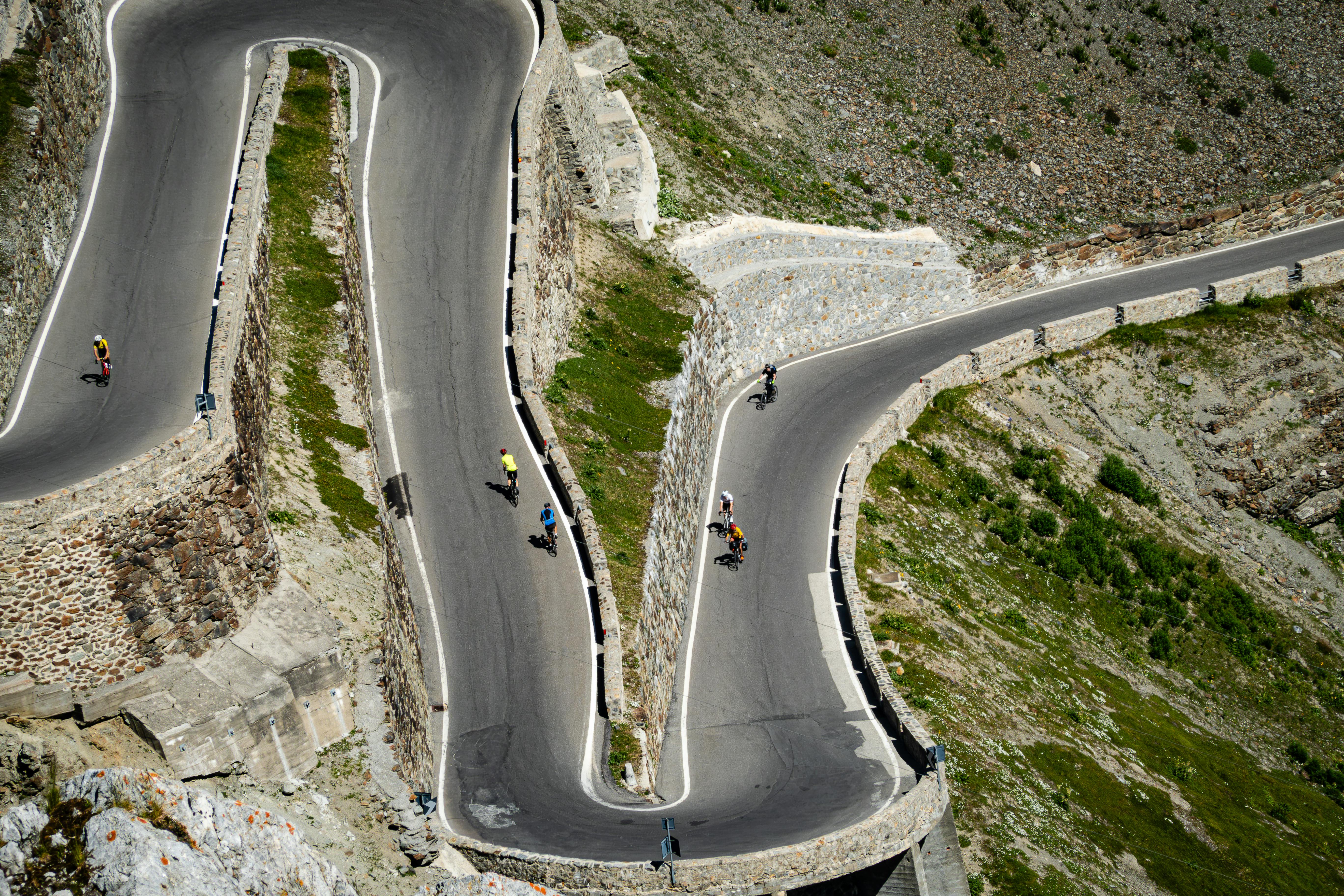 Cyclists biking along winding mountain road curves with scenic views.