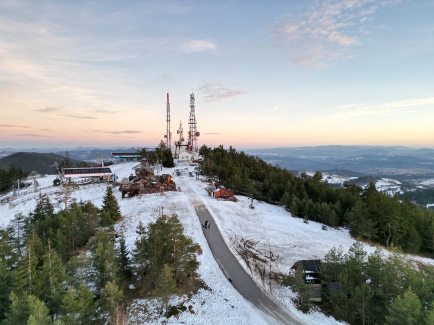 Aerial view of Zlatibor, Serbia with snow-covered terrain and communication towers at sunset.