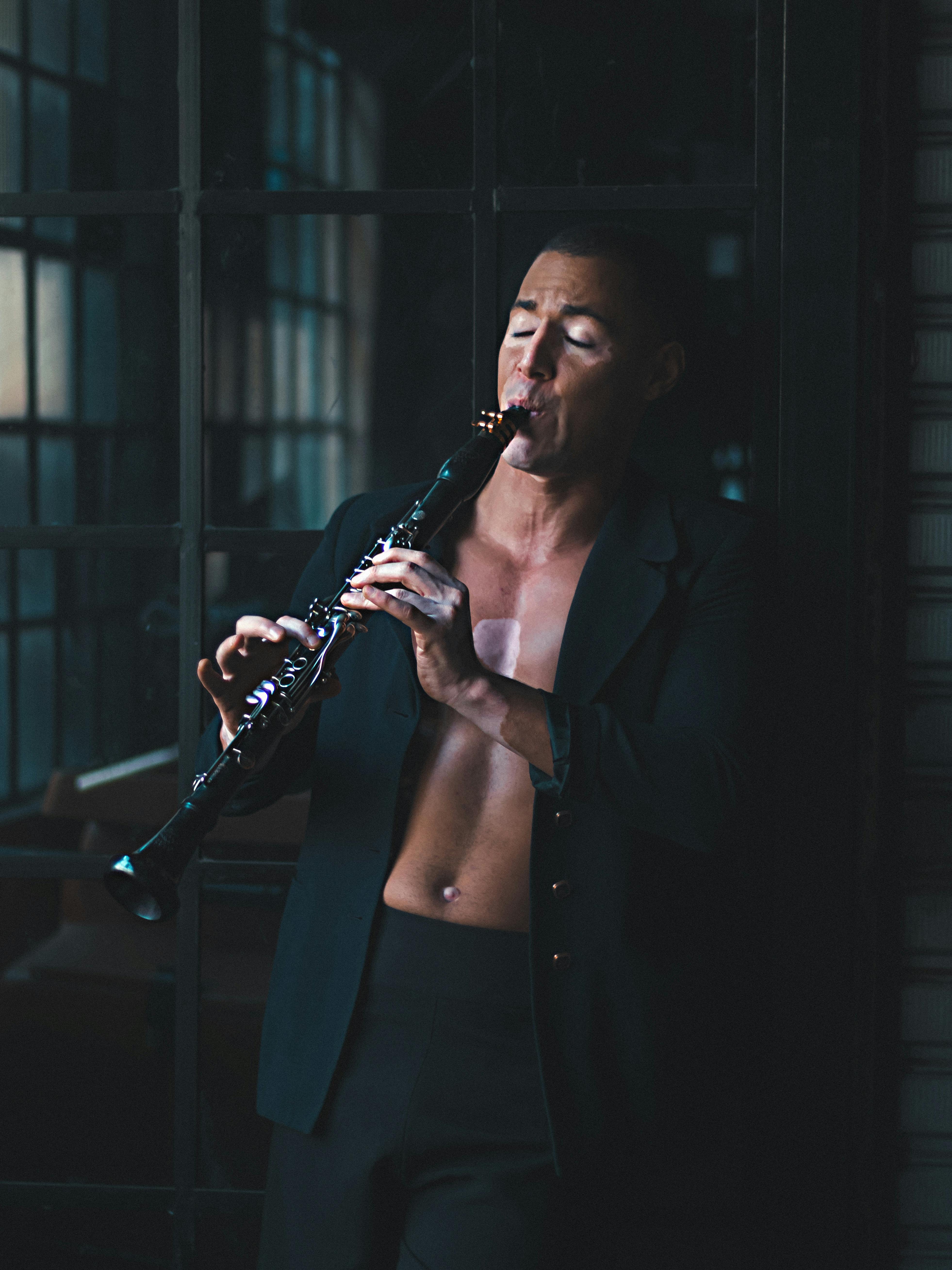 A male musician passionately plays a clarinet in an intimate indoor setting.