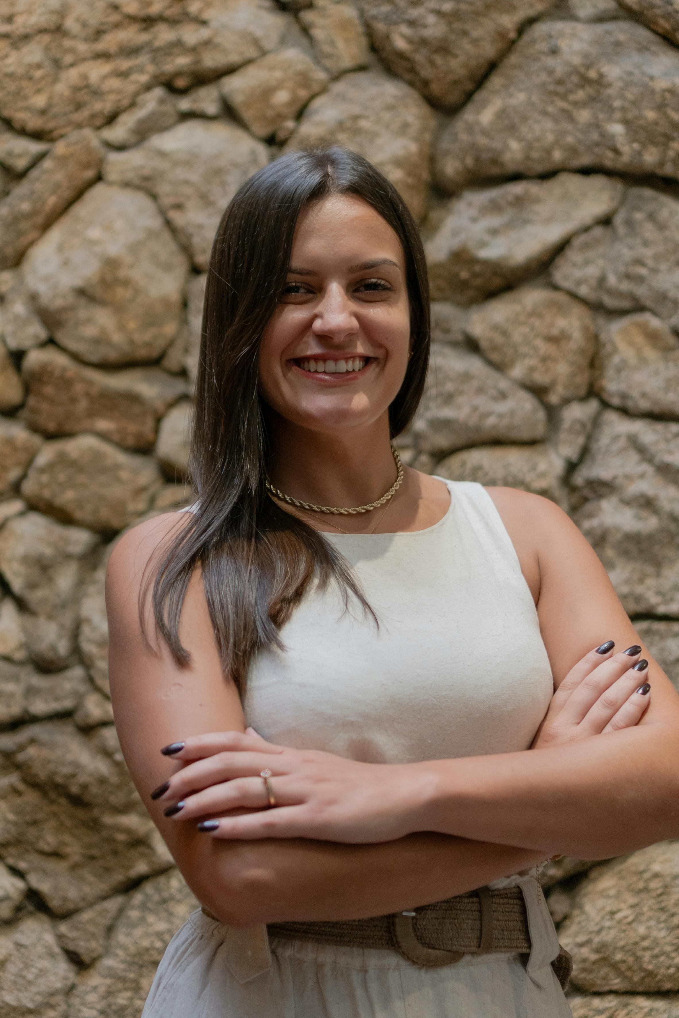 Smiling woman in a white dress poses confidently against a textured stone wall.