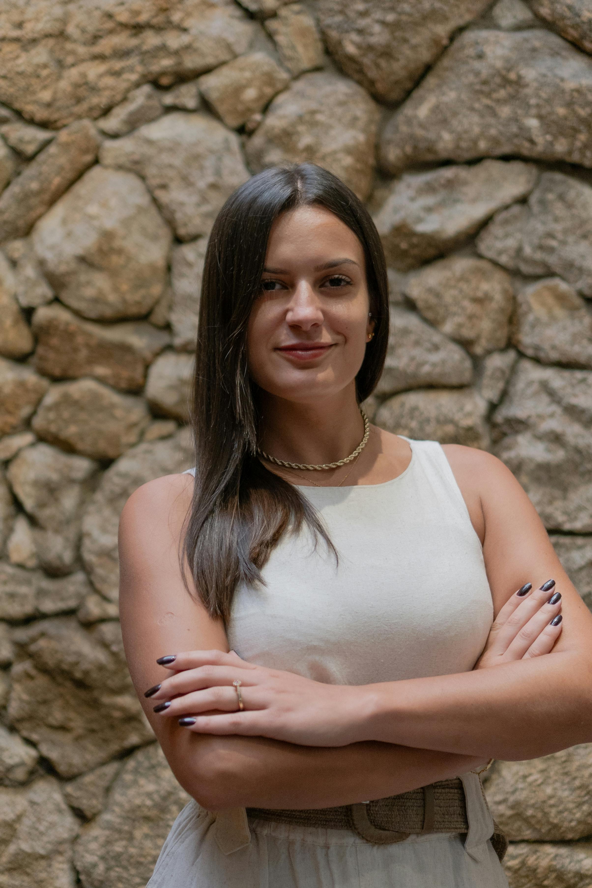 Portrait of a confident woman standing with arms crossed against a rustic stone wall background.