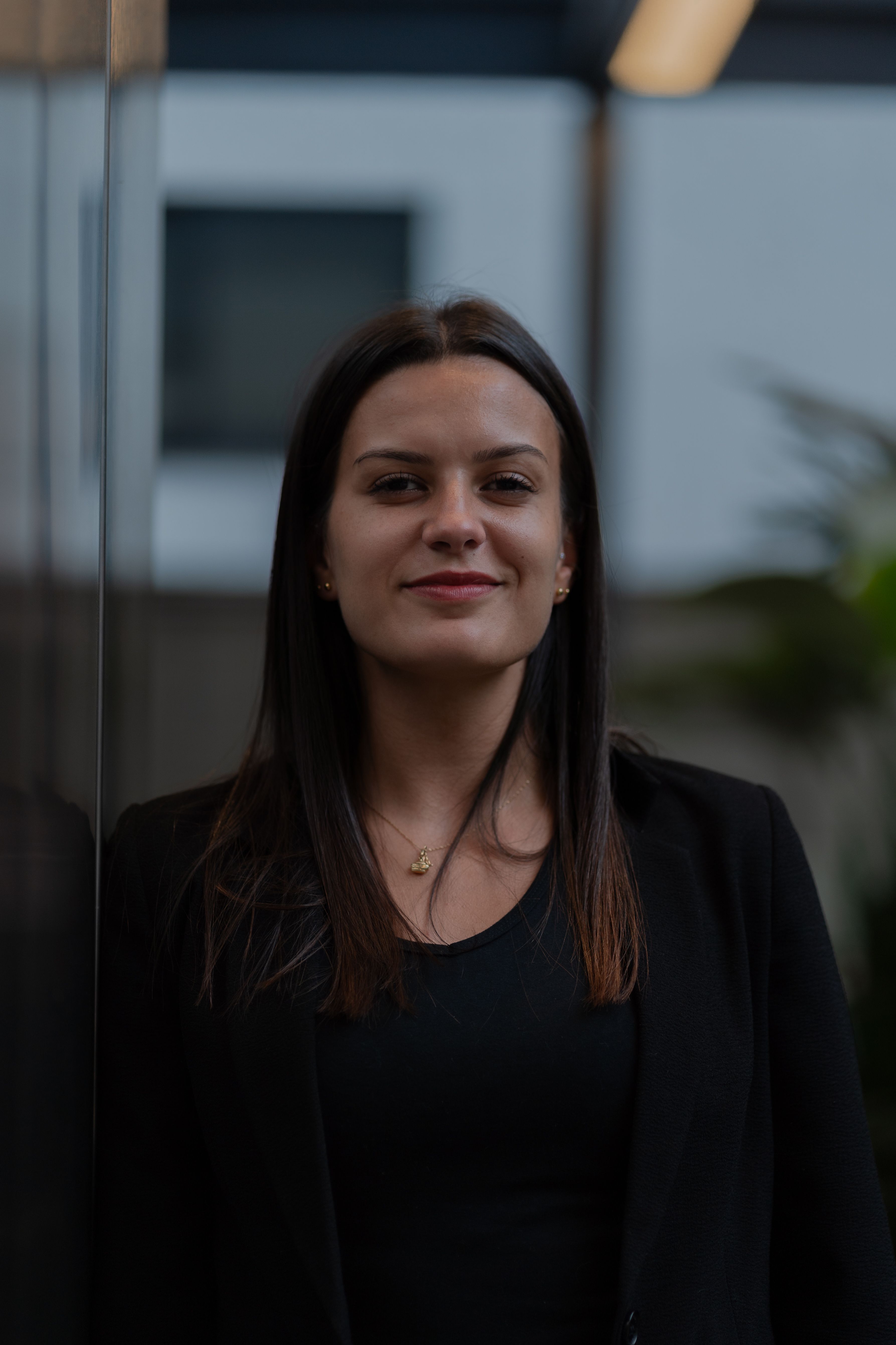 Close-up portrait of a confident young woman in a black suit indoors.