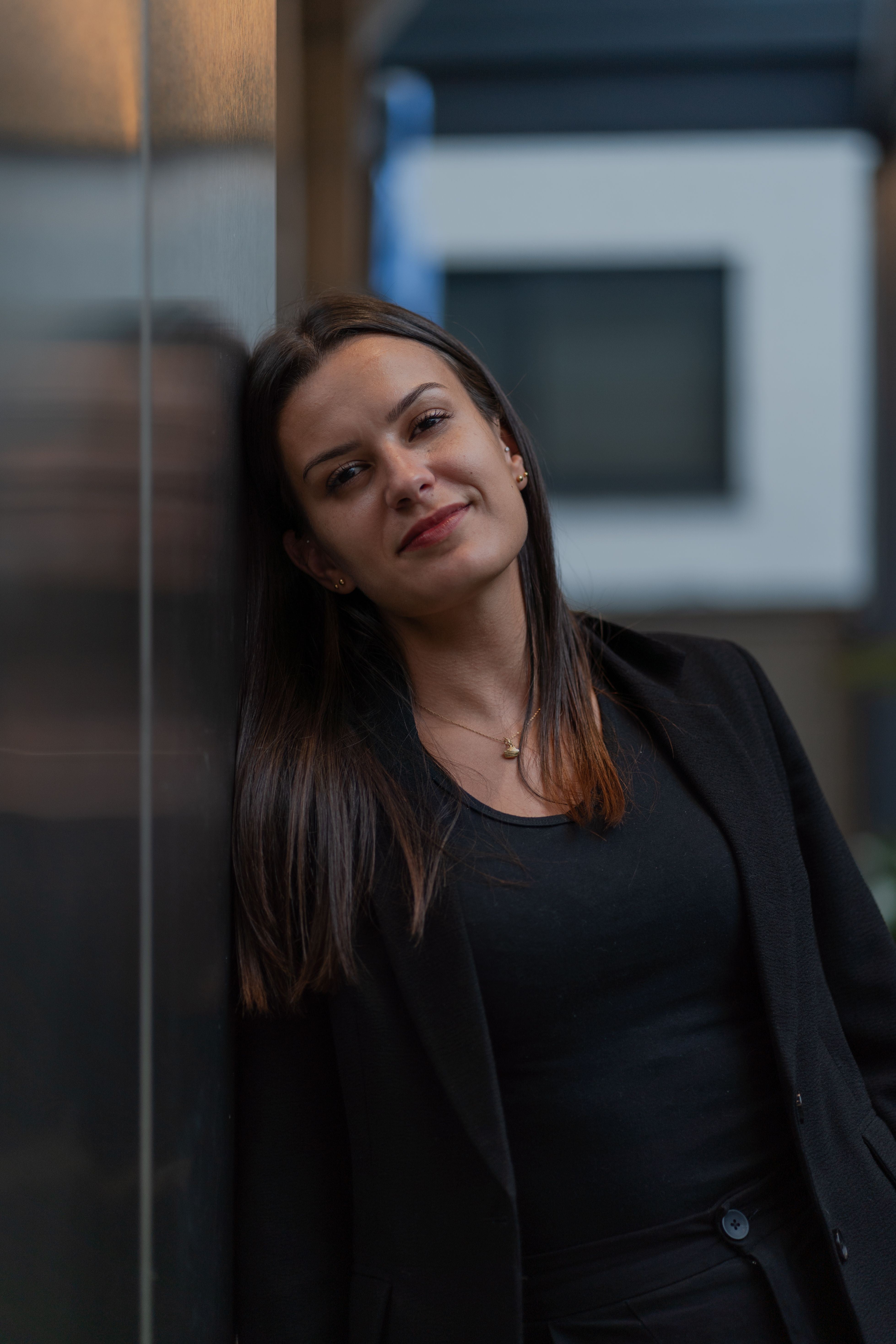 Portrait of a young woman leaning against a wall, expressing confidence and calmness.