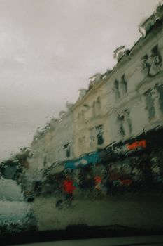 Artistic view of a cityscape through a car window with raindrops creating a blurred effect.