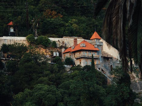 Rustic stone house with red roof amidst dense green forest in Gagra, showcasing serene beauty.