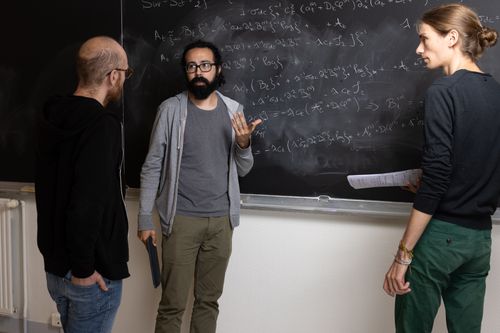 Free Three adults solving complex mathematical equations on a chalkboard indoors. Stock Photo