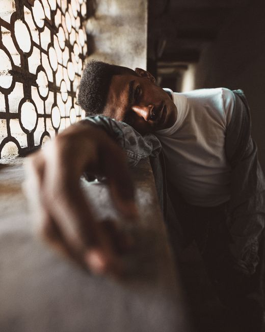Striking portrait of a man leaning on a window, showcasing moody lighting and artistic composition.