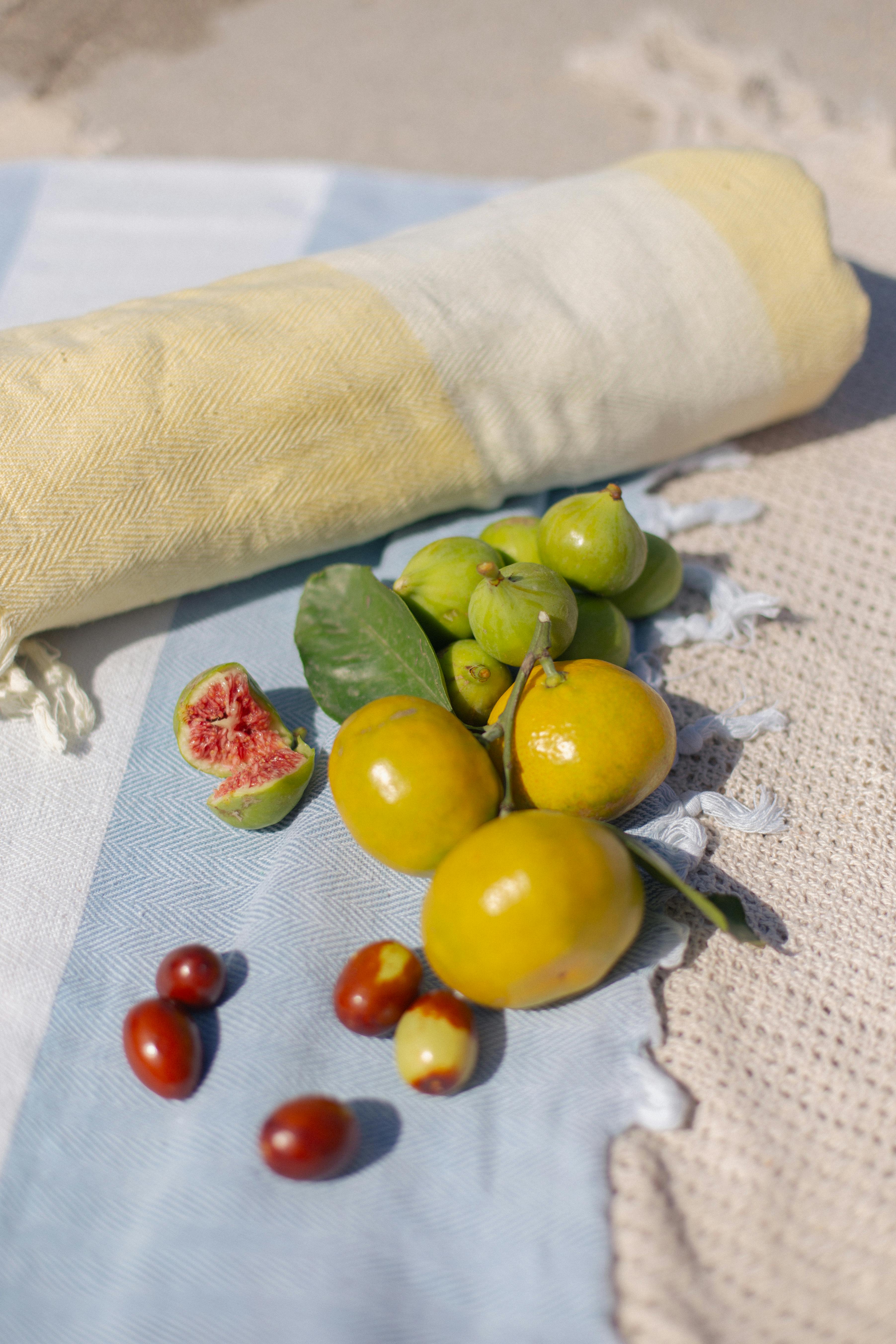 A colorful arrangement of figs, limes, and other fruits on a sunny beach towel setting.