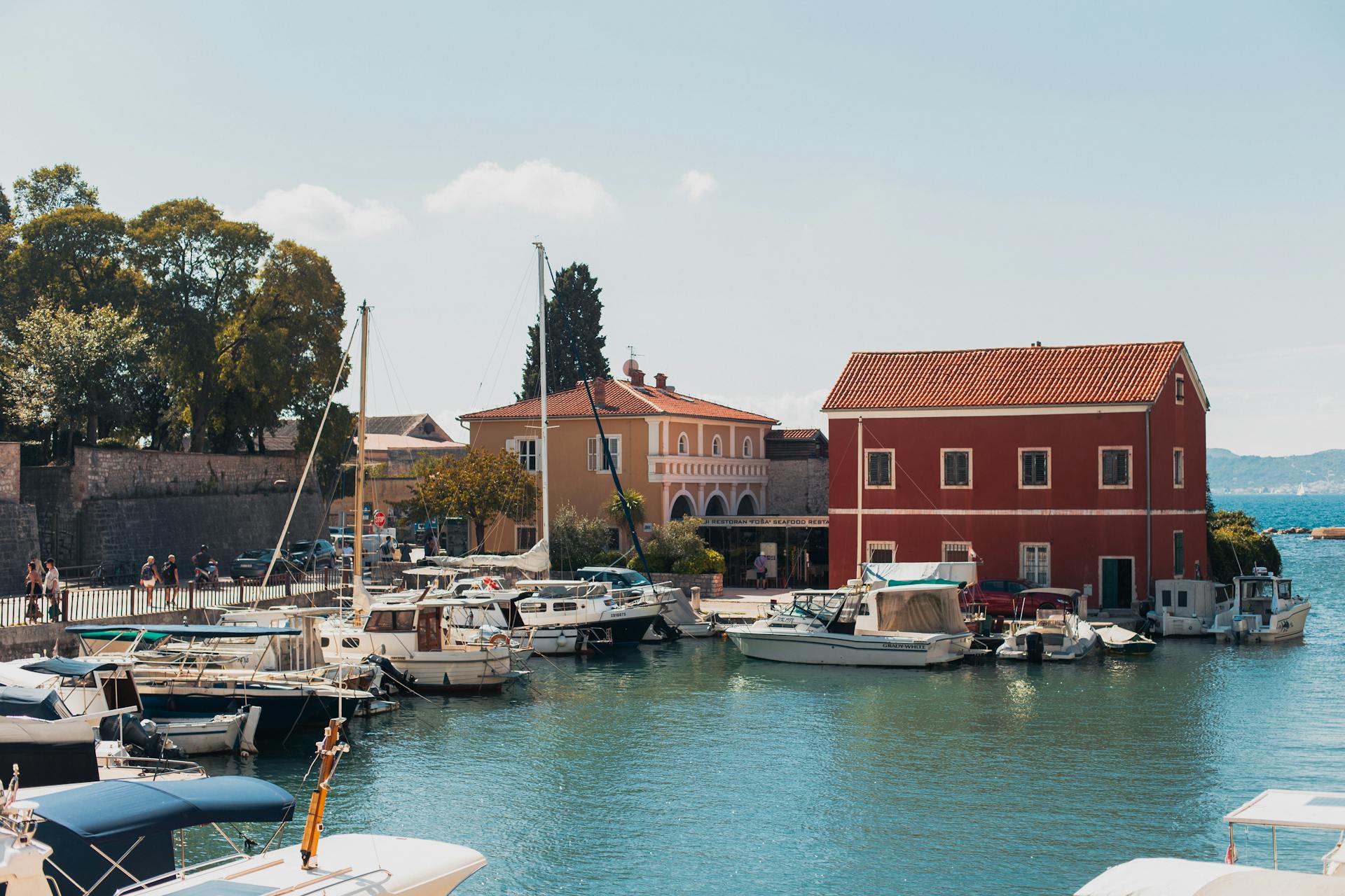 Boats docked in Zadar harbor with vibrant summer backdrop and charming architecture.