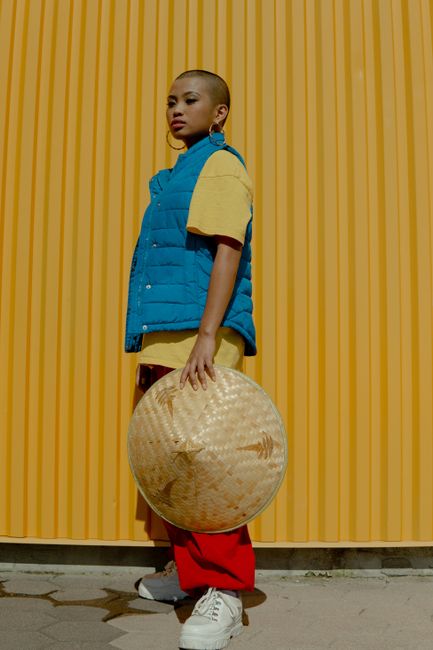 Fashionable woman posing with a straw hat against a vibrant yellow background.