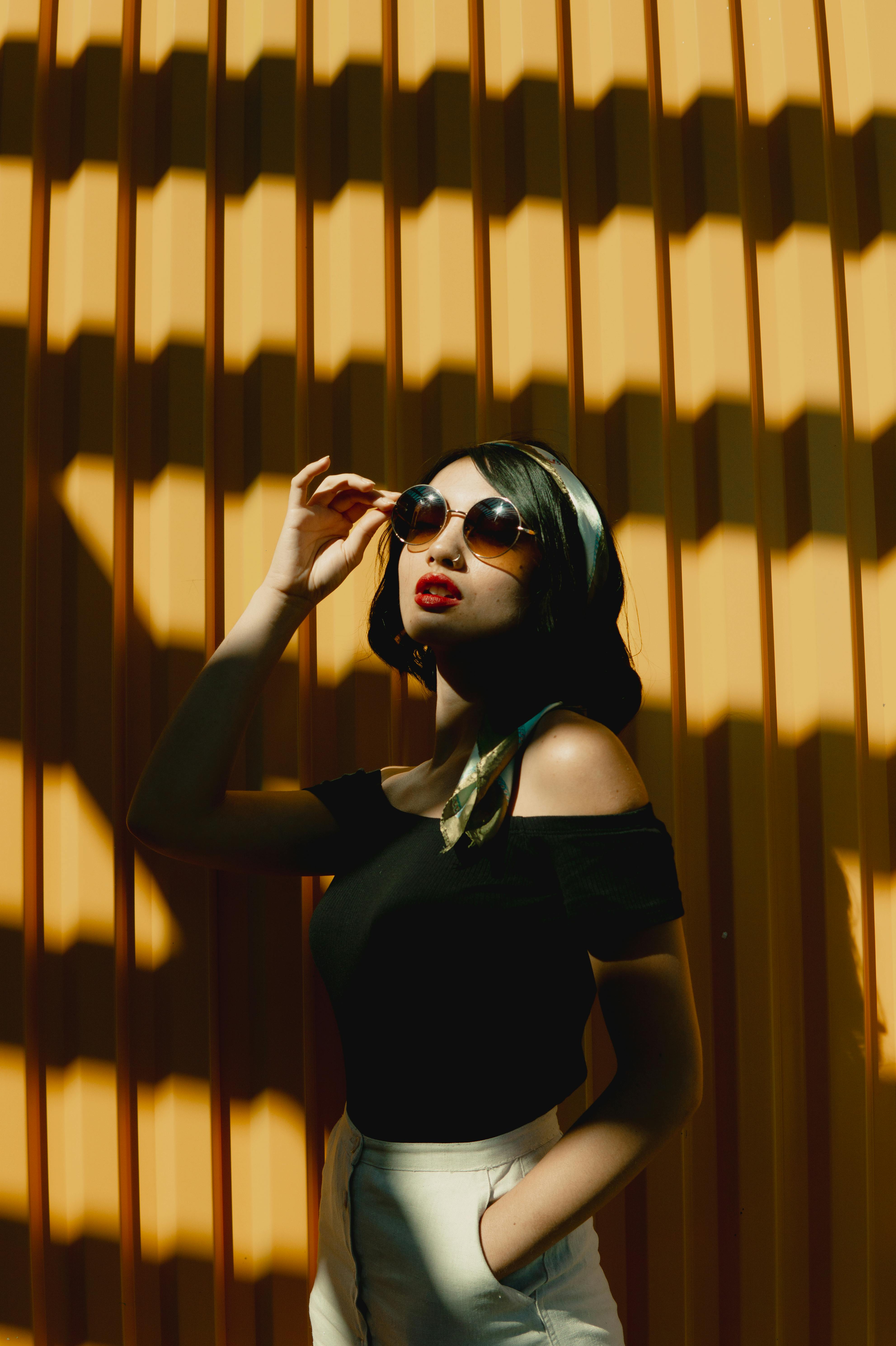 Fashionable woman with red lips and sunglasses posing elegantly in sunlight.