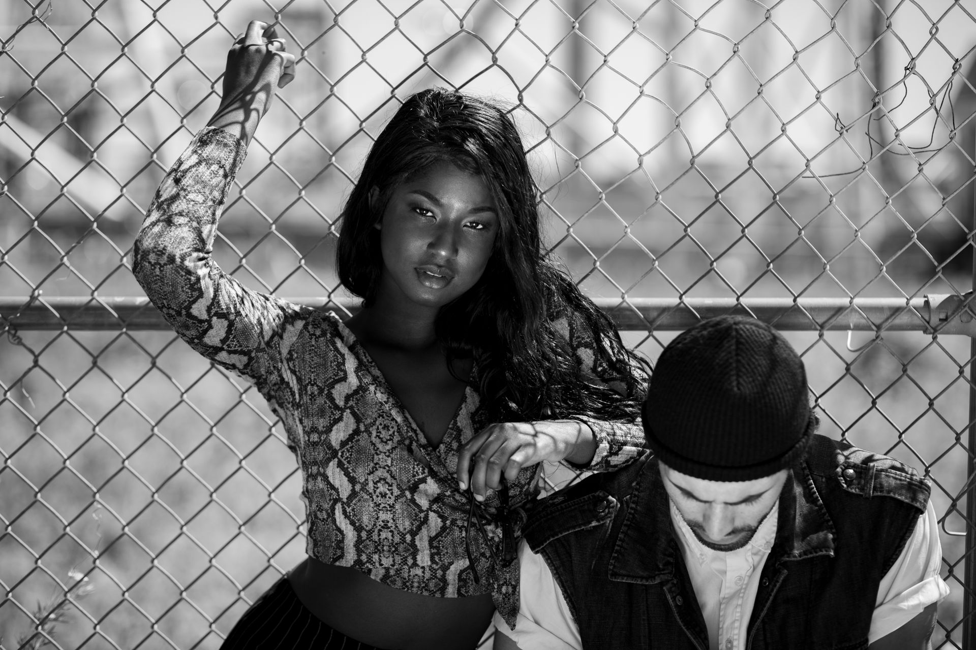 Stylish black and white portrait of two models posing outdoors by a fence.