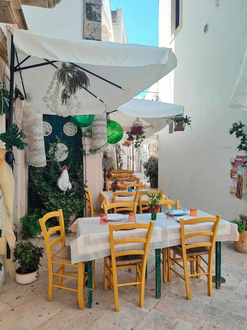 Free Rustic outdoor cafe in Cisternino, Italy with vibrant chairs and greenery. Stock Photo