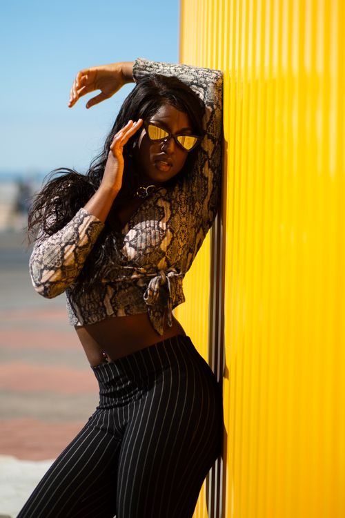 Free Fashionable African woman in sunglasses leaning against a yellow wall outdoors. Stock Photo