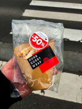 Close-up of a chicken curry wrap with 50% discount packaging held outdoors.