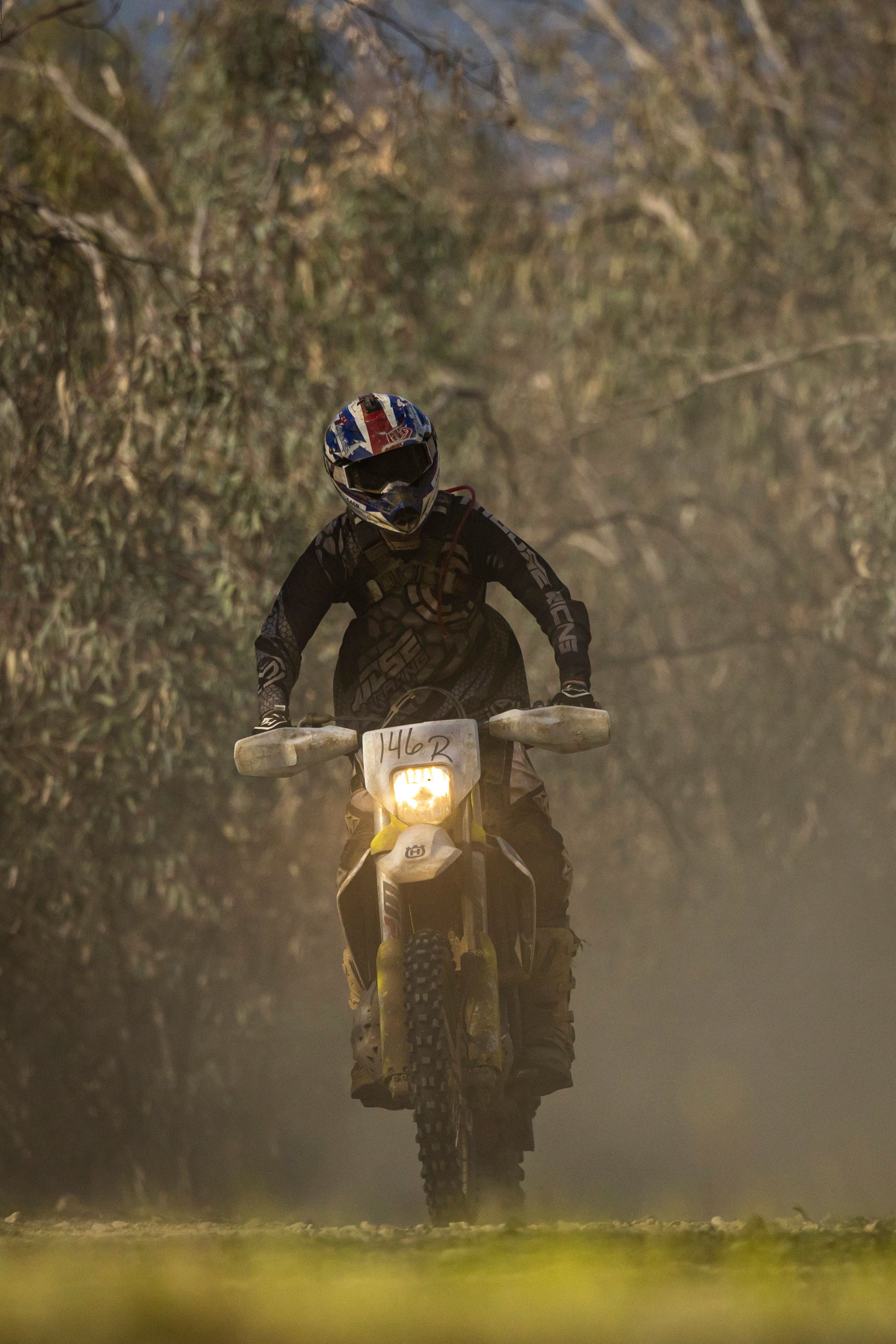 A motocross rider speeds through a dusty forest path on a dirt bike, creating a thrilling scene.