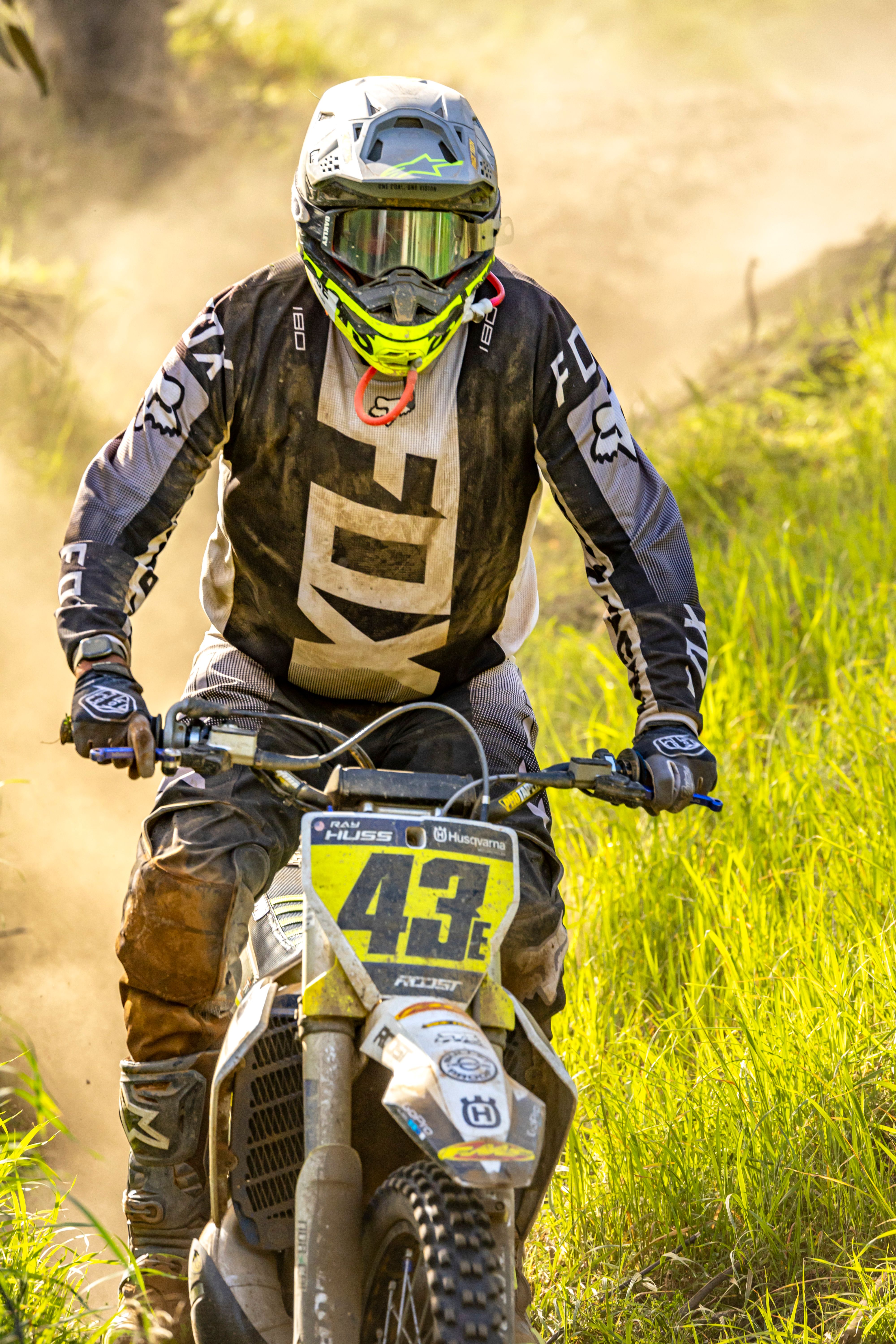 Racer in full gear on a dirt bike tearing through a grassy trail, capturing the essence of extreme racing.