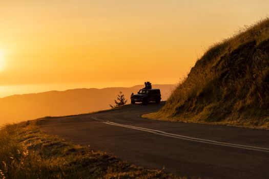 A car enjoys a peaceful sunset drive on a winding hilltop road with scenic mountain views.