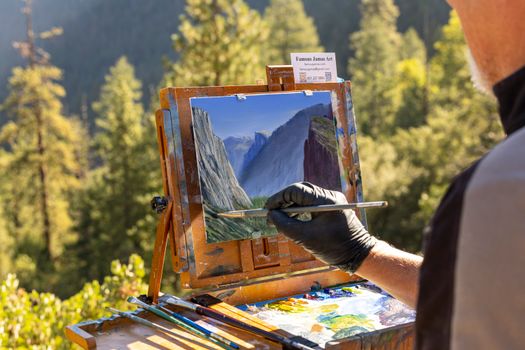 Artist painting a realistic Yosemite landscape in nature, capturing scenic beauty.