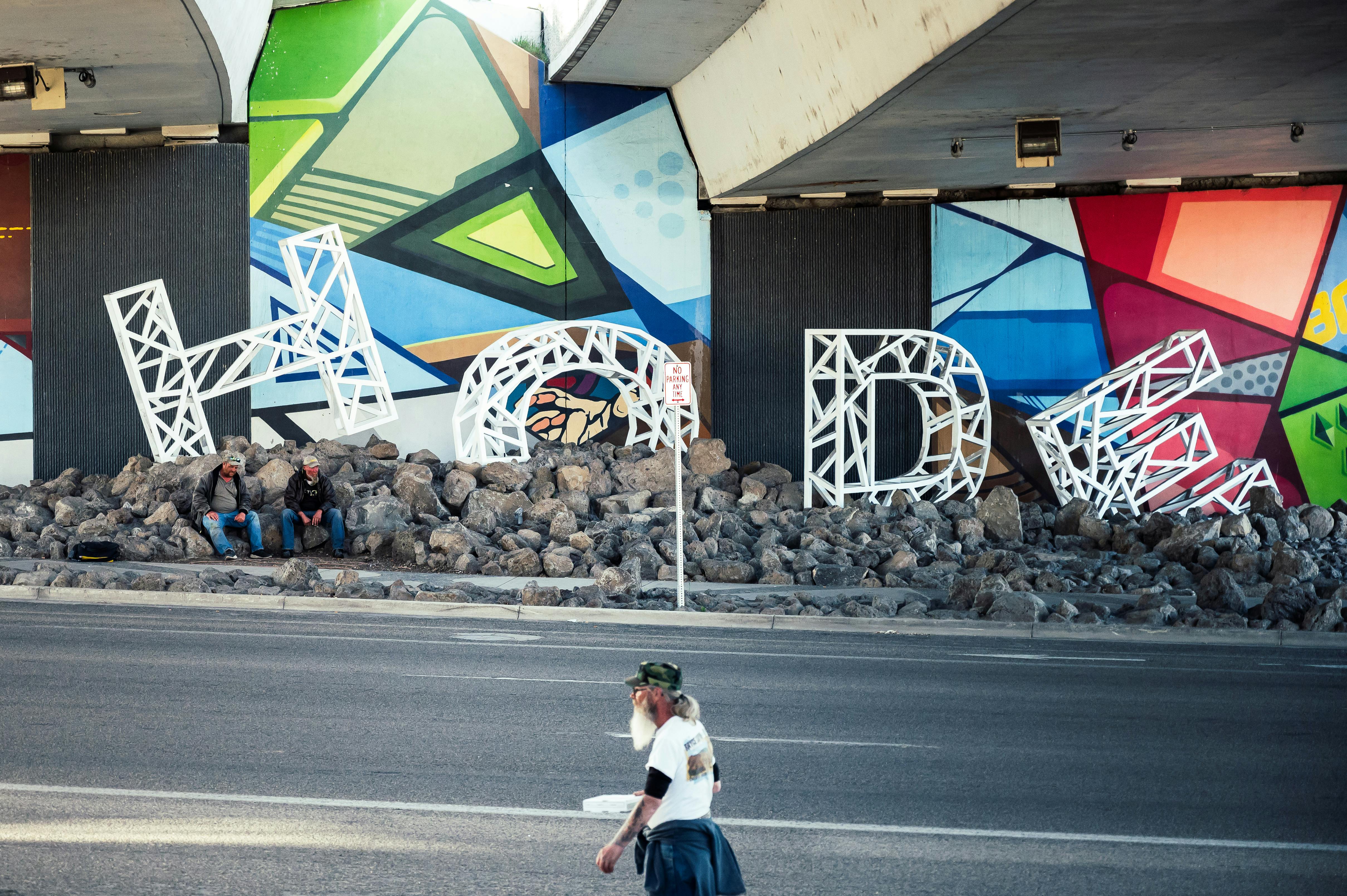 Vibrant graffiti and steel letters beneath a highway highlight urban life.