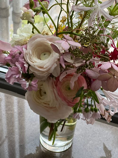 Free A vibrant mix of spring flowers in a glass vase by a window. Stock Photo
