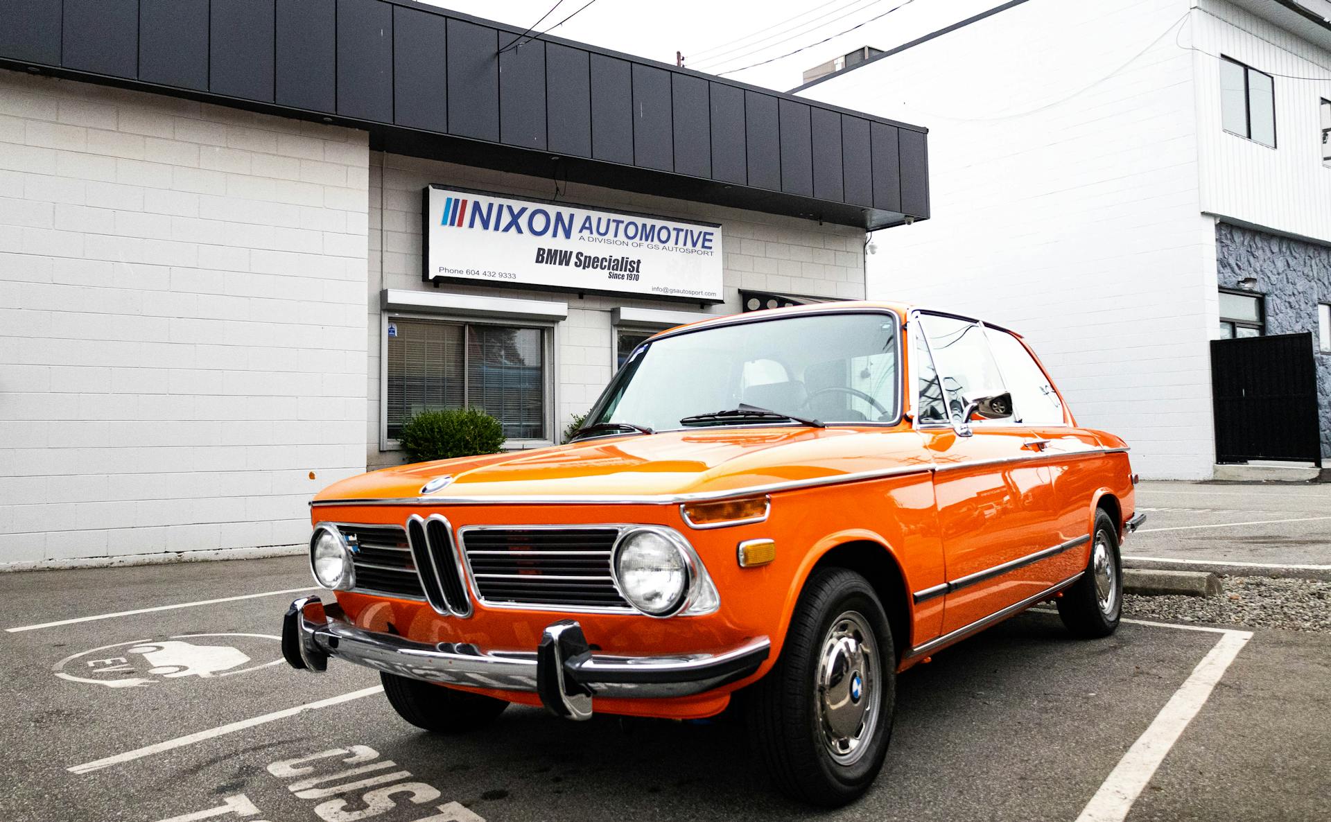 A classic bright orange BMW parked outside Nixon Automotive, a BMW specialist shop.