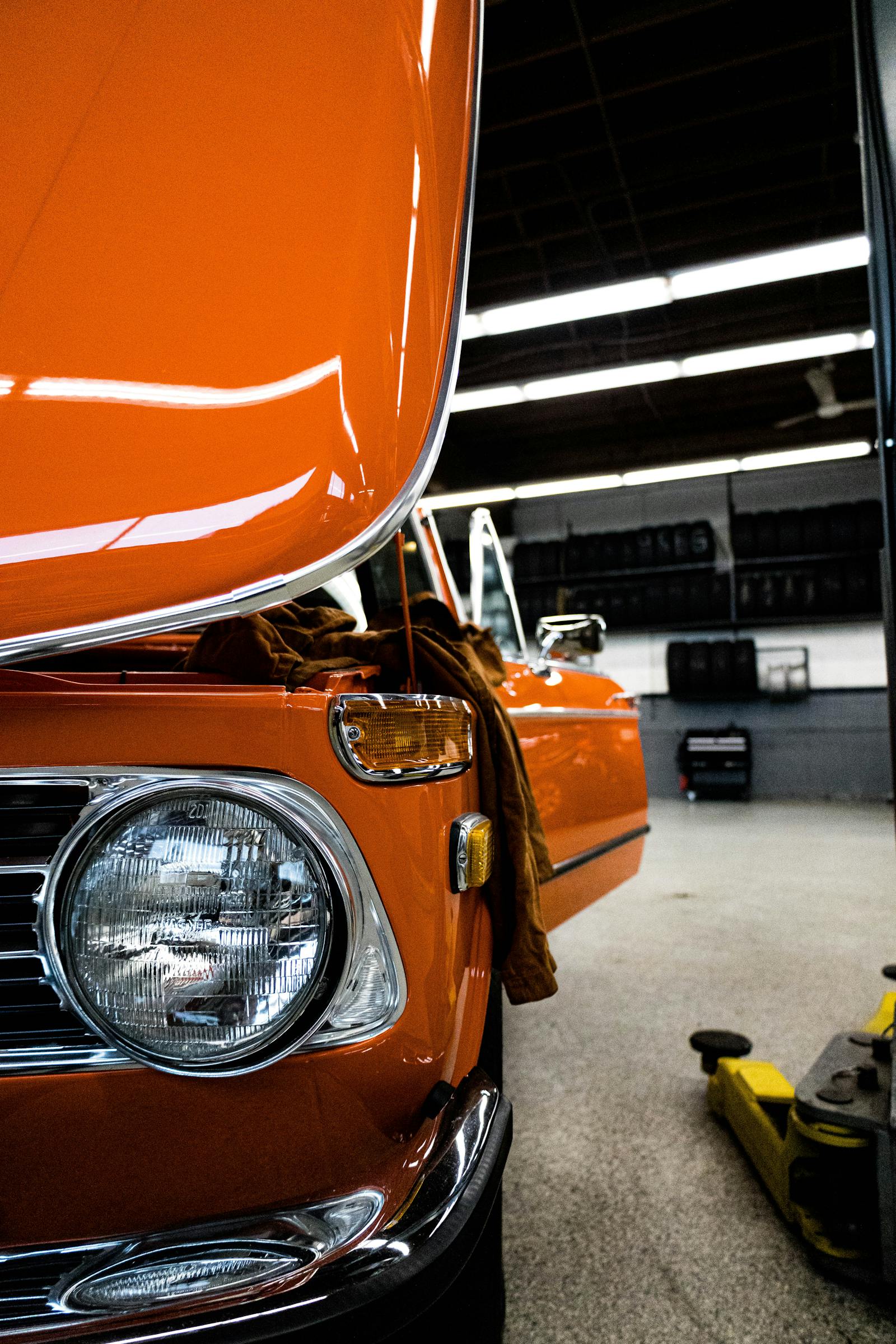 Bright orange classic car with hood open in a workshop.