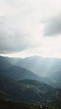 A stunning view of sun rays piercing through clouds over lush green mountains, creating a serene atmosphere.