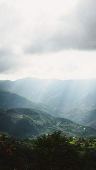 Sun rays streaming through clouds over a lush green mountain valley, creating a serene and peaceful landscape.