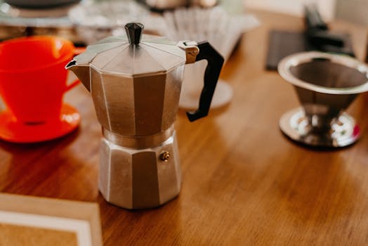 High-angle view of a classic Italian moka pot surrounded by coffee accessories on a wooden table.