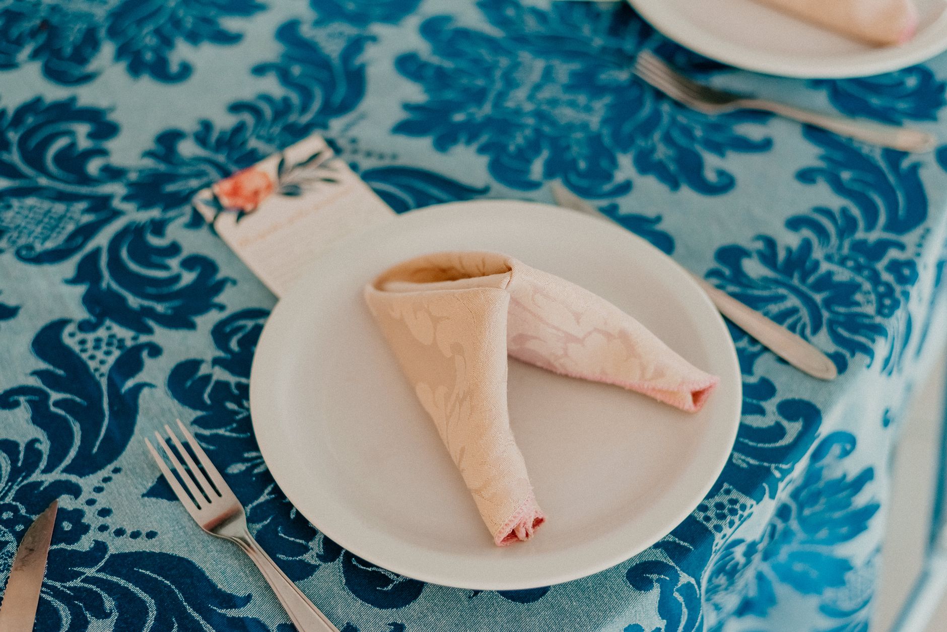 A beautifully composed dining table setting with a folded napkin and floral tablecloth.