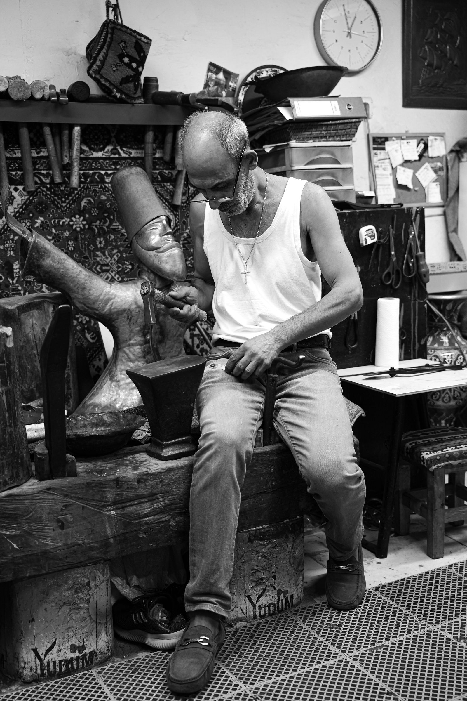 Metalworker shaping a bronze sculpture by hand in a crowded workshop