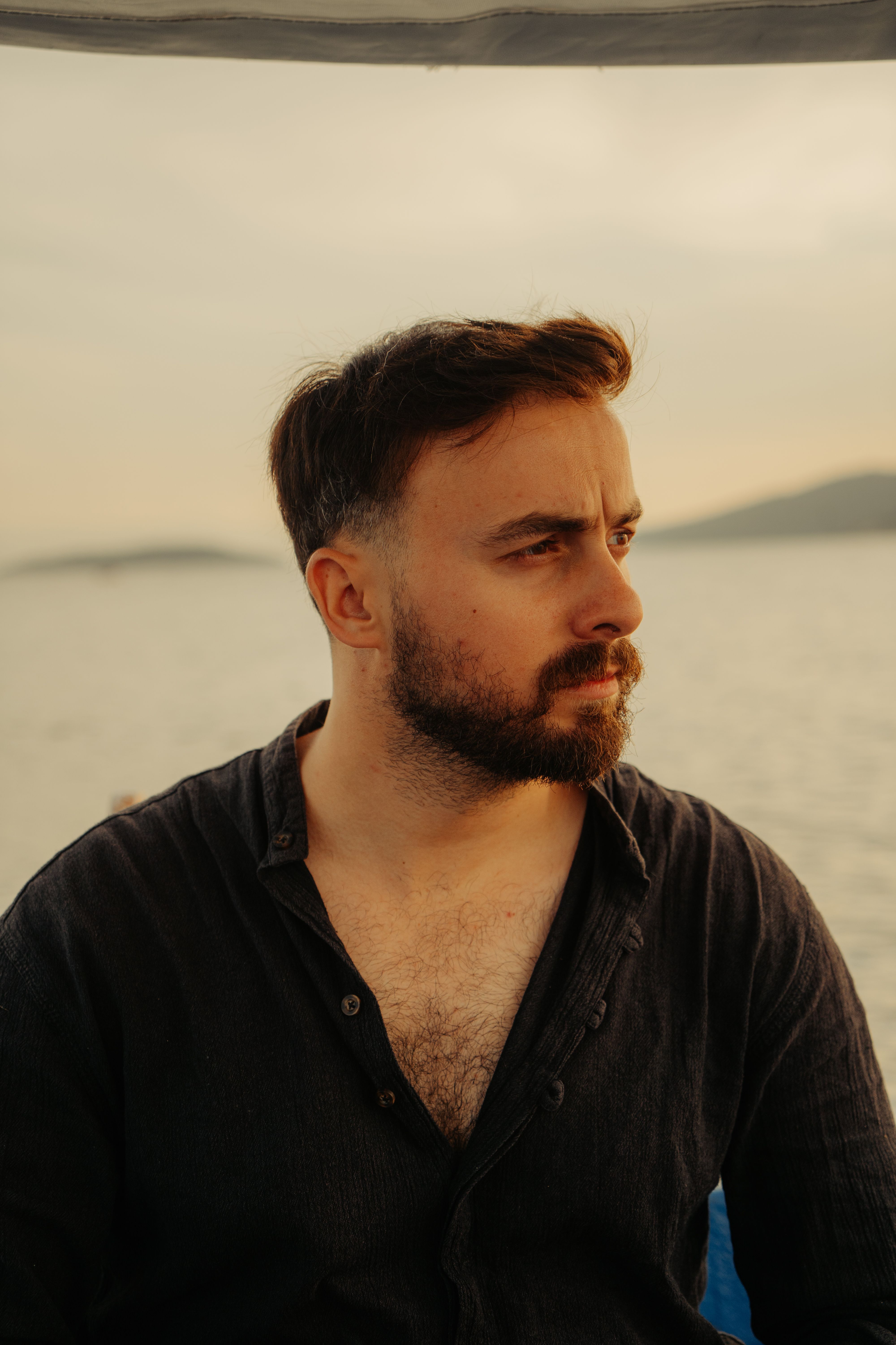 A young man in a contemplative mood gazes over a tranquil lake at sunset, capturing a moment of peace.