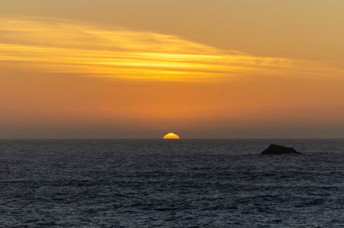 Free Hypnotic sunset over the ocean horizon with vibrant orange sky and calm waves. Stock Photo