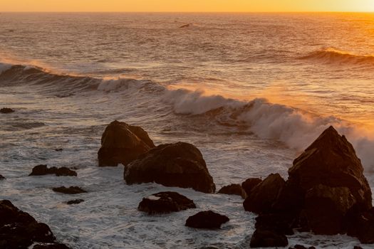 Powerful ocean waves crashing against rocks during a vibrant sunset, creating a dramatic seascape.