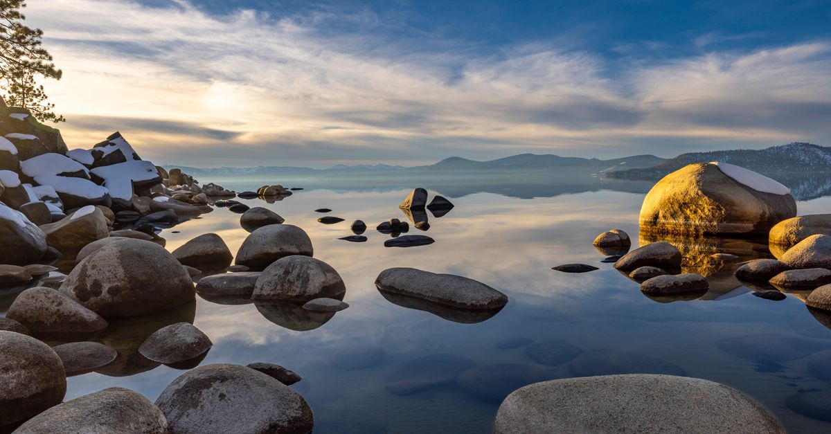 Scenic view of a rocky lake shore with reflections on a calm day in winter.