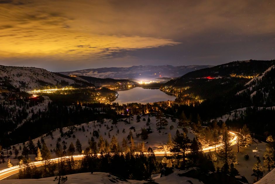 Breathtaking night shot of Donner Lake illuminated, surrounded by snow-covered mountains.