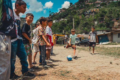 Free A group of children playing soccer on a dirt field in a rural village setting. Stock Photo