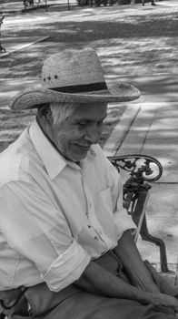 A joyful elderly man in a hat smiling on a bench in sunny Cholula, Puebla, Mexico.