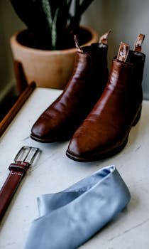 Brown leather boots paired with a blue tie and belt on a marble surface, showcasing classic men's fashion.