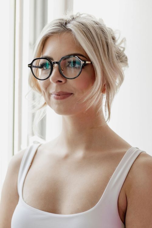 Free Elegant portrait of a woman with round glasses gazing out of a window, embodying modern fashion and style. Stock Photo
