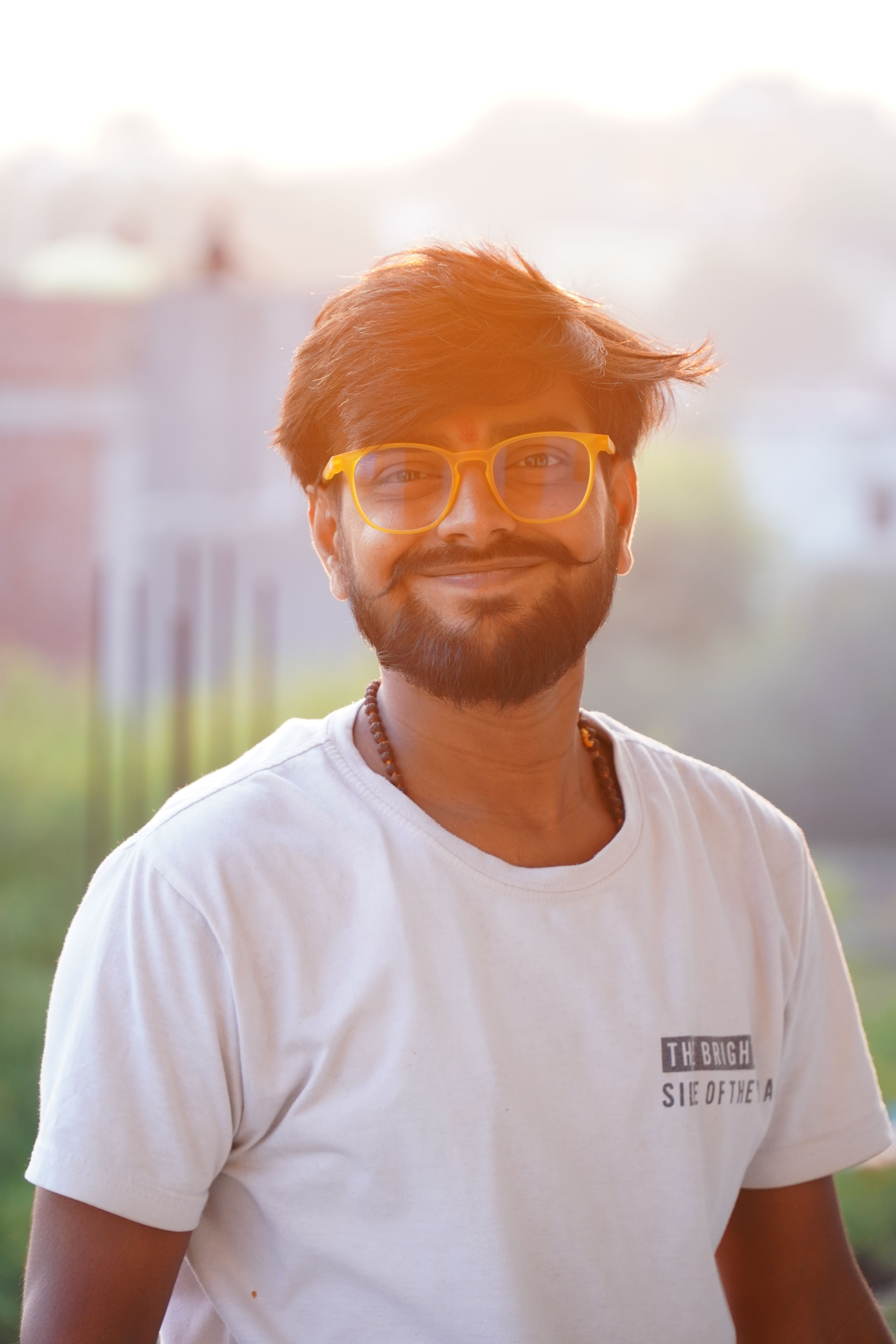 Young man with glasses smiling warmly outdoors during sunset in Varanasi.