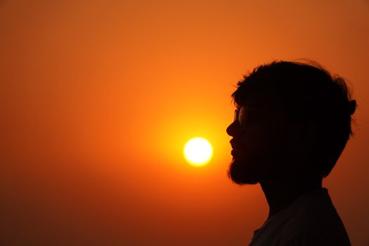 Silhouette of a man against a vibrant orange sunset sky, capturing a serene and contemplative moment.