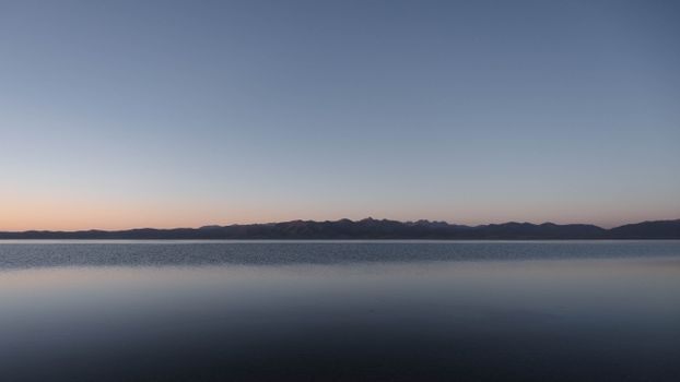 Peaceful sunset with serene mountains reflecting on a calm lake.