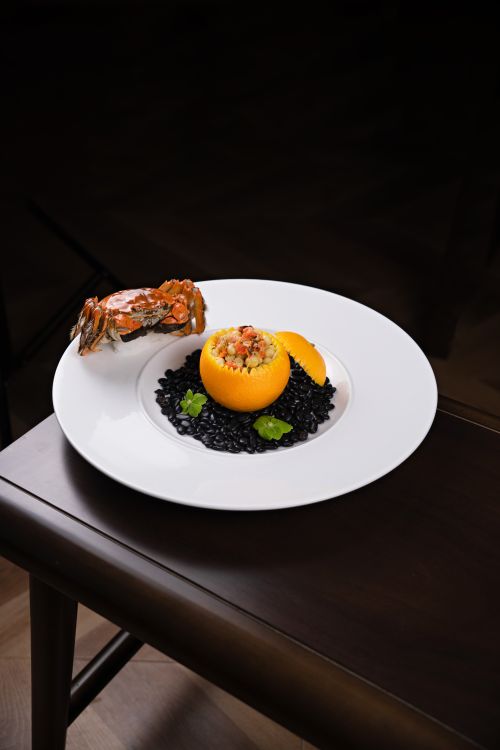 Free Elegant seafood dish featuring lemon, black rice, and garnished crab served on a white plate. Stock Photo